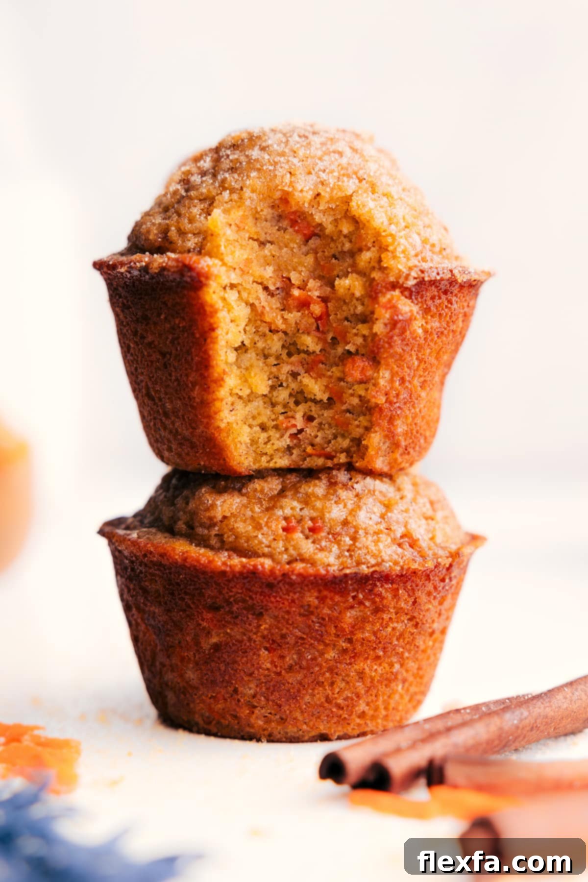 Stacked healthy carrot muffins with a bite taken out of the top one, revealing its soft, tender, and moist interior with flecks of grated carrot.