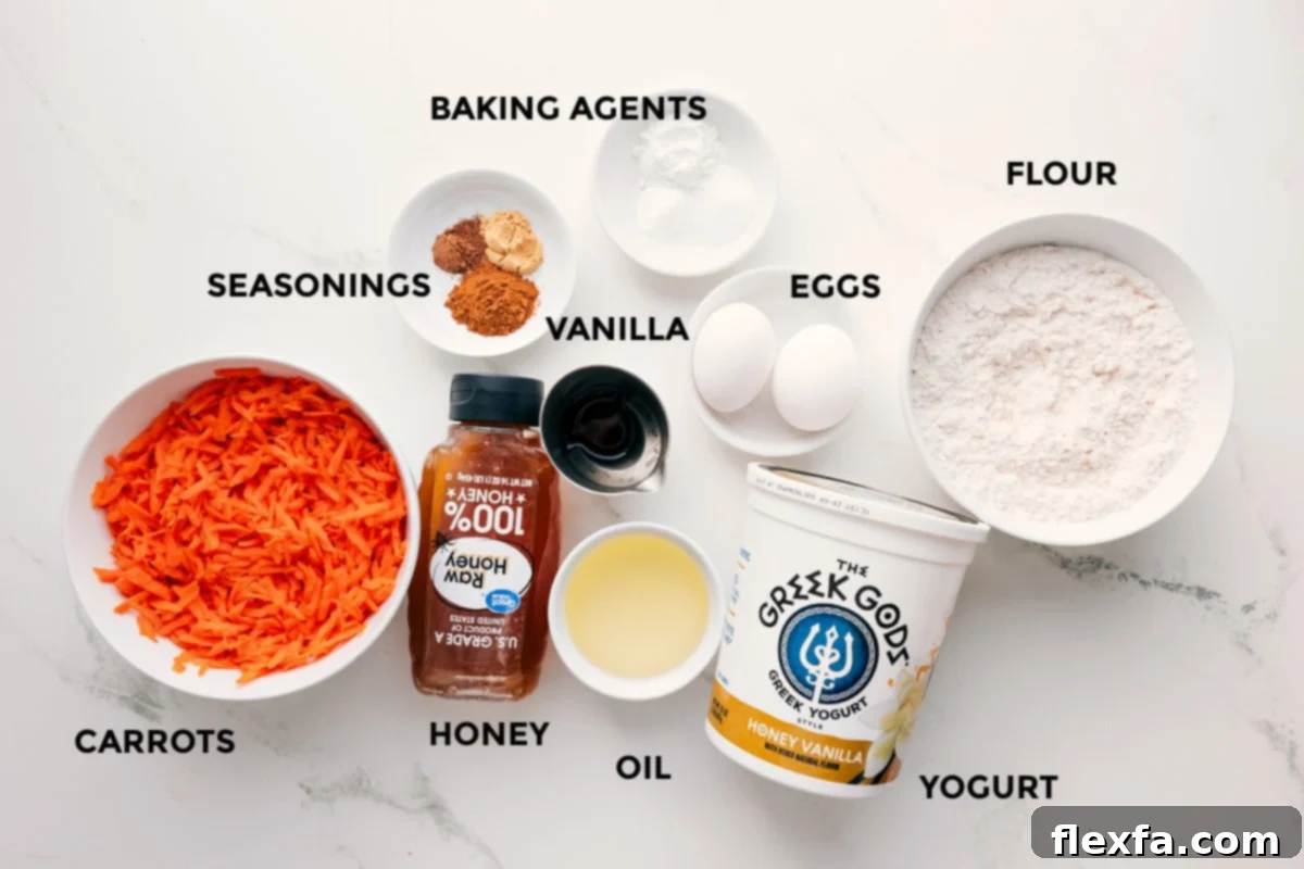 All the fresh ingredients for healthy carrot muffins are neatly arranged on a counter, including grated carrots, spices, honey, coconut oil, Greek yogurt, eggs, vanilla extract, flour, baking soda, and baking powder.
