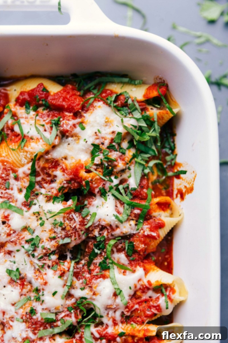 A baking dish filled with cheesy Stuffed Shells with Sausage, golden brown and bubbling, garnished with fresh basil.