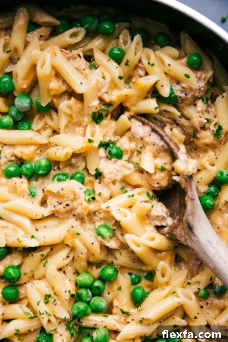 A creamy Tuna Pasta dish with green peas and a cheesy sauce, scooped with a spoon from a skillet.