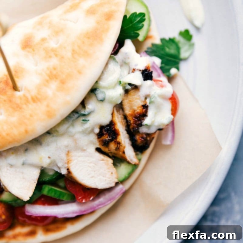A fully assembled Greek chicken gyro, overflowing with grilled chicken, fresh vegetables, and creamy tzatziki sauce in a soft pita.