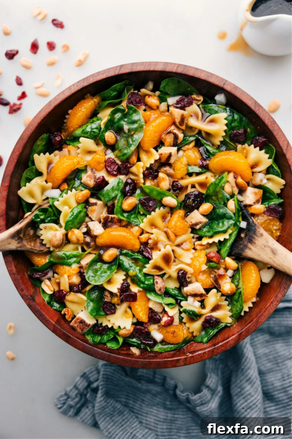 A large bowl of teriyaki chicken salad, featuring pasta, spinach, nuts, oranges, water chestnuts, sweet onion, and tender chicken with a 3-ingredient dressing.