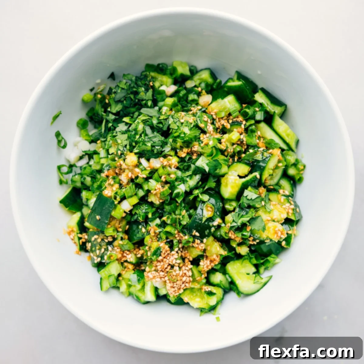 Smashed Cucumber Salad in a mixing bowl with dressing and fresh herbs, ready to be thoroughly tossed together for maximum flavor.