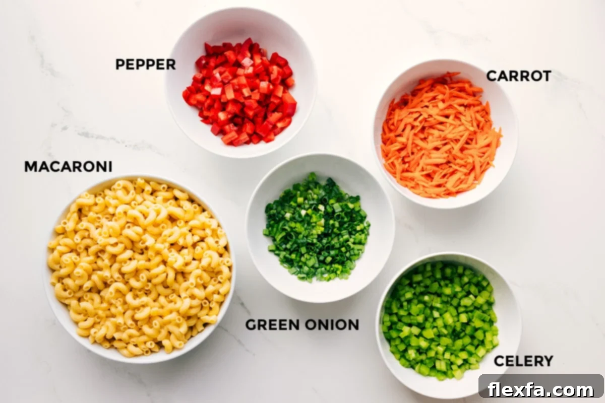A vibrant display of fresh ingredients for macaroni salad, including cooked macaroni, diced red bell pepper, shredded carrots, chopped green onions, and finely diced celery, all prepped and ready for mixing.