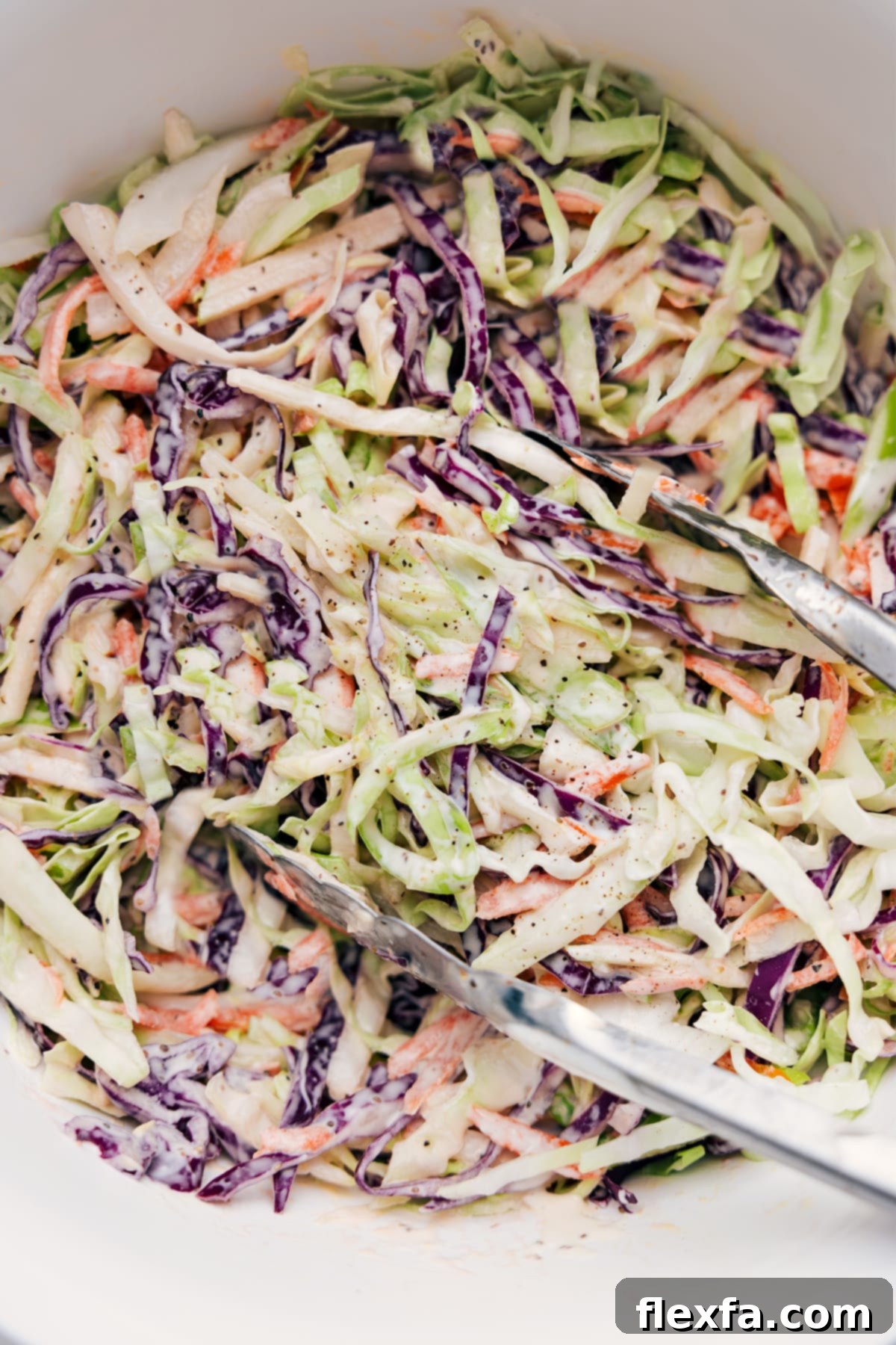 Easy Coleslaw Recipe being tossed in a creamy dressing, with tongs lifting a large scoop, showcasing its fresh and vibrant appearance.