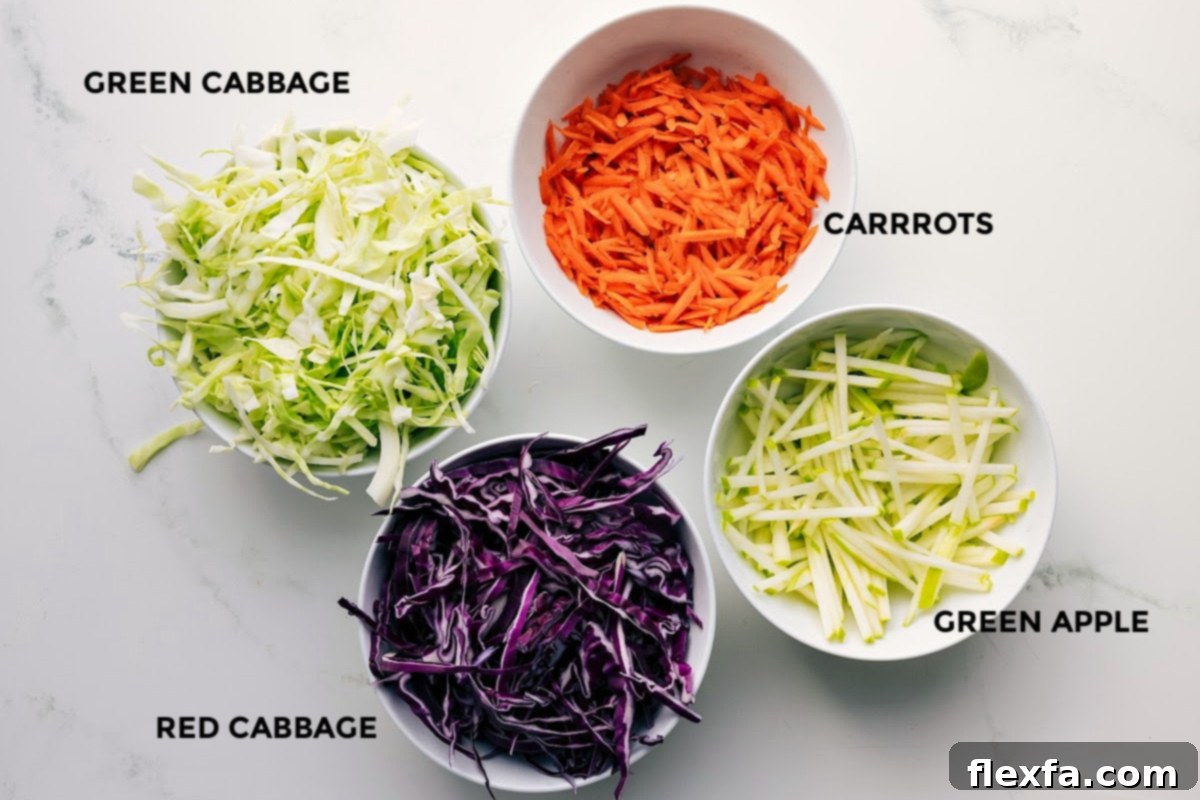 The vibrant ingredients for the Easy Coleslaw Recipe laid out, including green cabbage, red cabbage, finely grated carrots, and thinly sliced green apple matchsticks.