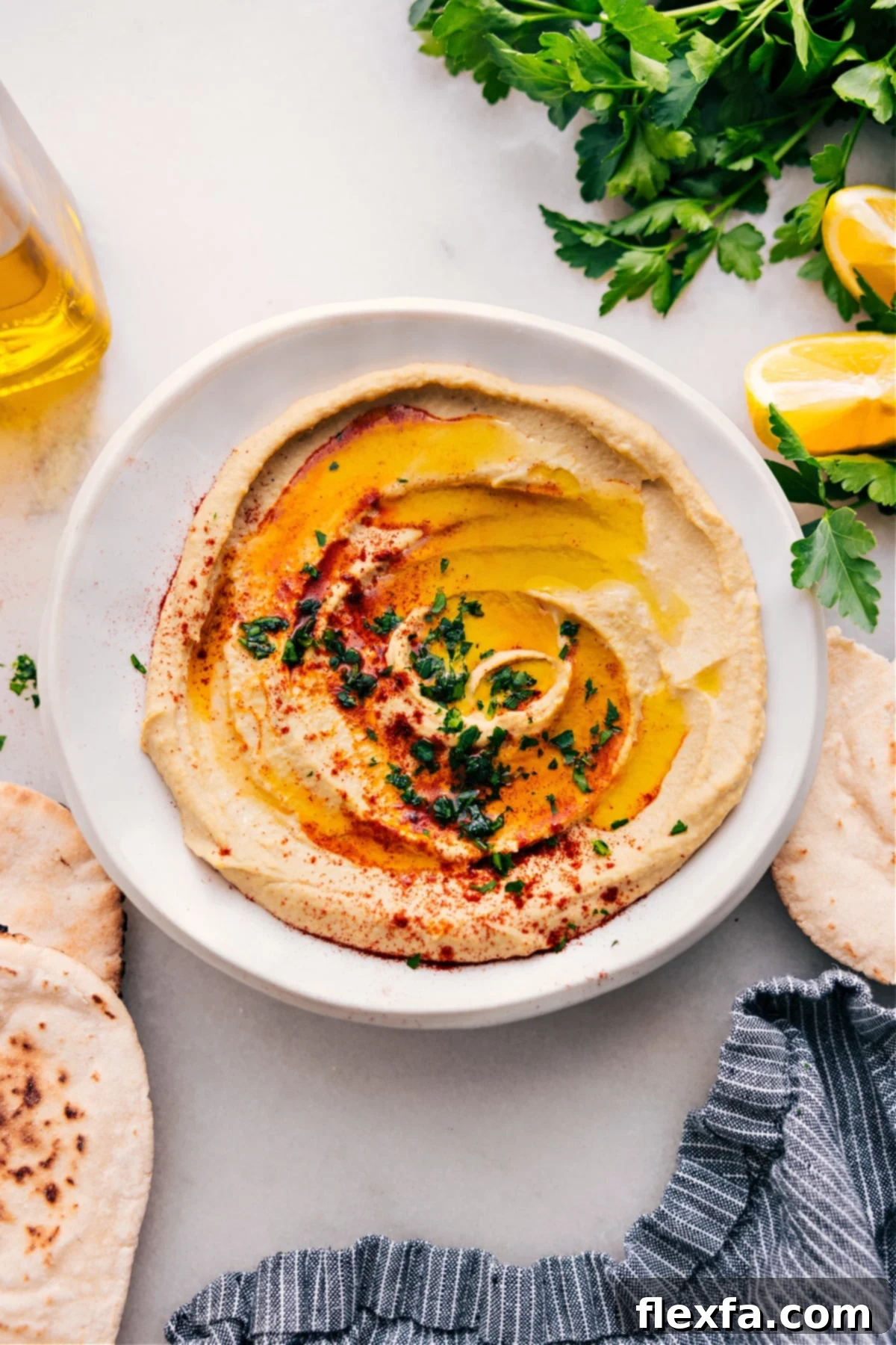 A beautifully presented bowl of creamy hummus, drizzled with olive oil, sprinkled with paprika, and garnished with fresh parsley.