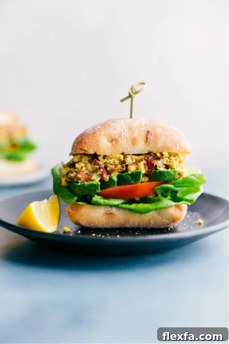 A delightful pesto chickpea sandwich on ciabatta bread, filled with mashed chickpeas, tomatoes, avocado, and lettuce.