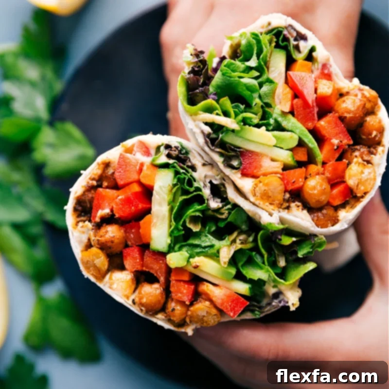 A wholesome hummus wrap, sliced in half, revealing a colorful filling of chickpeas, fresh vegetables, and creamy hummus.