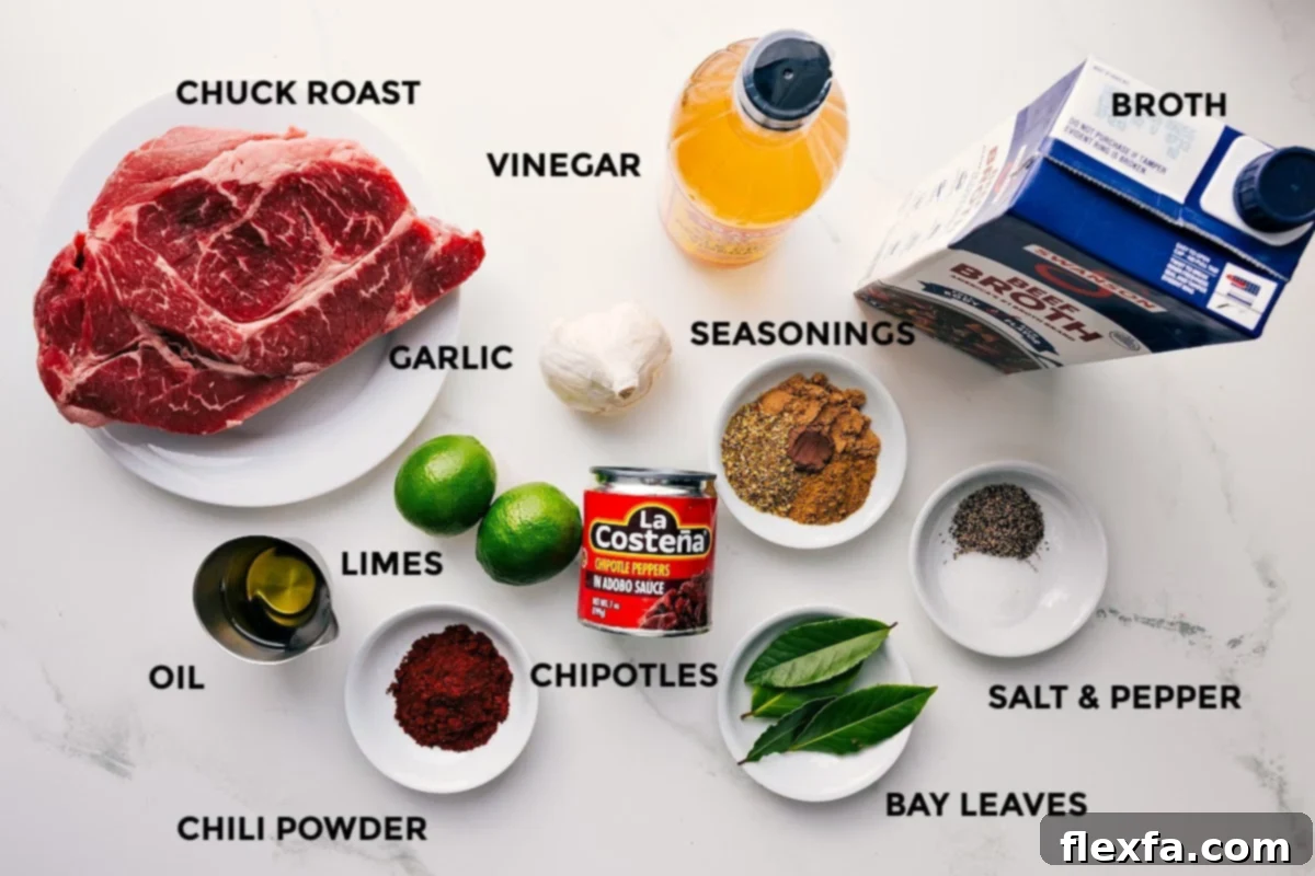 An overhead shot of all the ingredients needed for Barbacoa Beef, including a chuck roast, spices, chipotles in adobo, beef broth, and fresh limes.