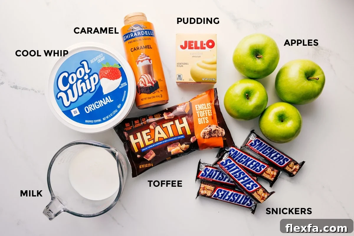 All the ingredients in this recipe prepped out for easy assembly including the milk, cool whip, caramel, toffee, snickers, apples, and jello.