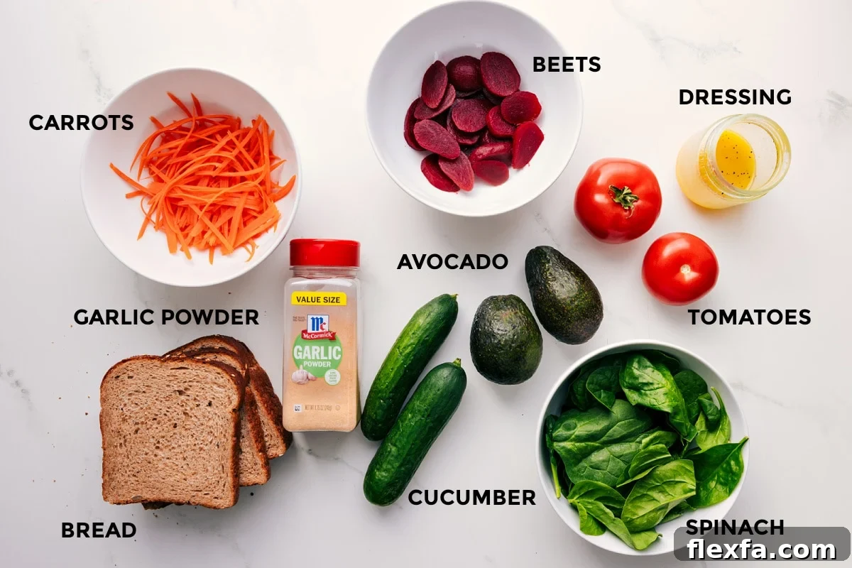 All the ingredients in this recipe prepped out for easy assembly including the carrots, garlic powder, bread, beets, avocado, cucumber, spinach, tomatoes, and dressing.