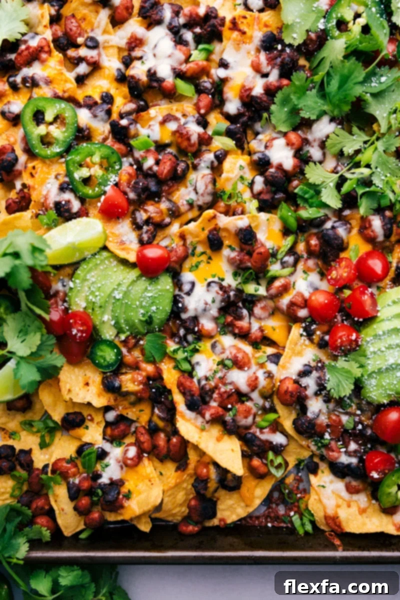 A sheet pan of vegetarian nachos loaded with melted cheese, beans, and fresh toppings.