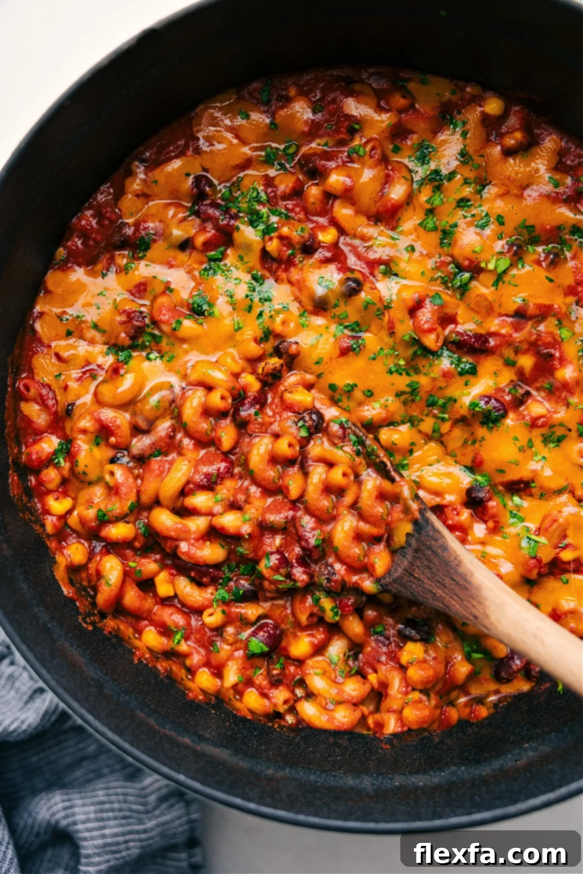 A large pot of vegetarian chili mac with melted cheese being scooped out.