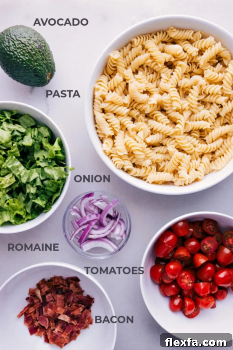 All the fresh ingredients for the BLT Pasta Salad laid out on a countertop, including pasta, bacon, lettuce, tomatoes, and avocados.
