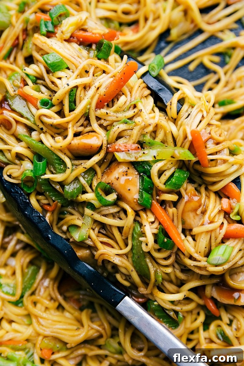 Asian chicken recipes: Chicken chow mein in a skillet with tongs, filled with fresh vegetables, perfectly cooked and seasoned.