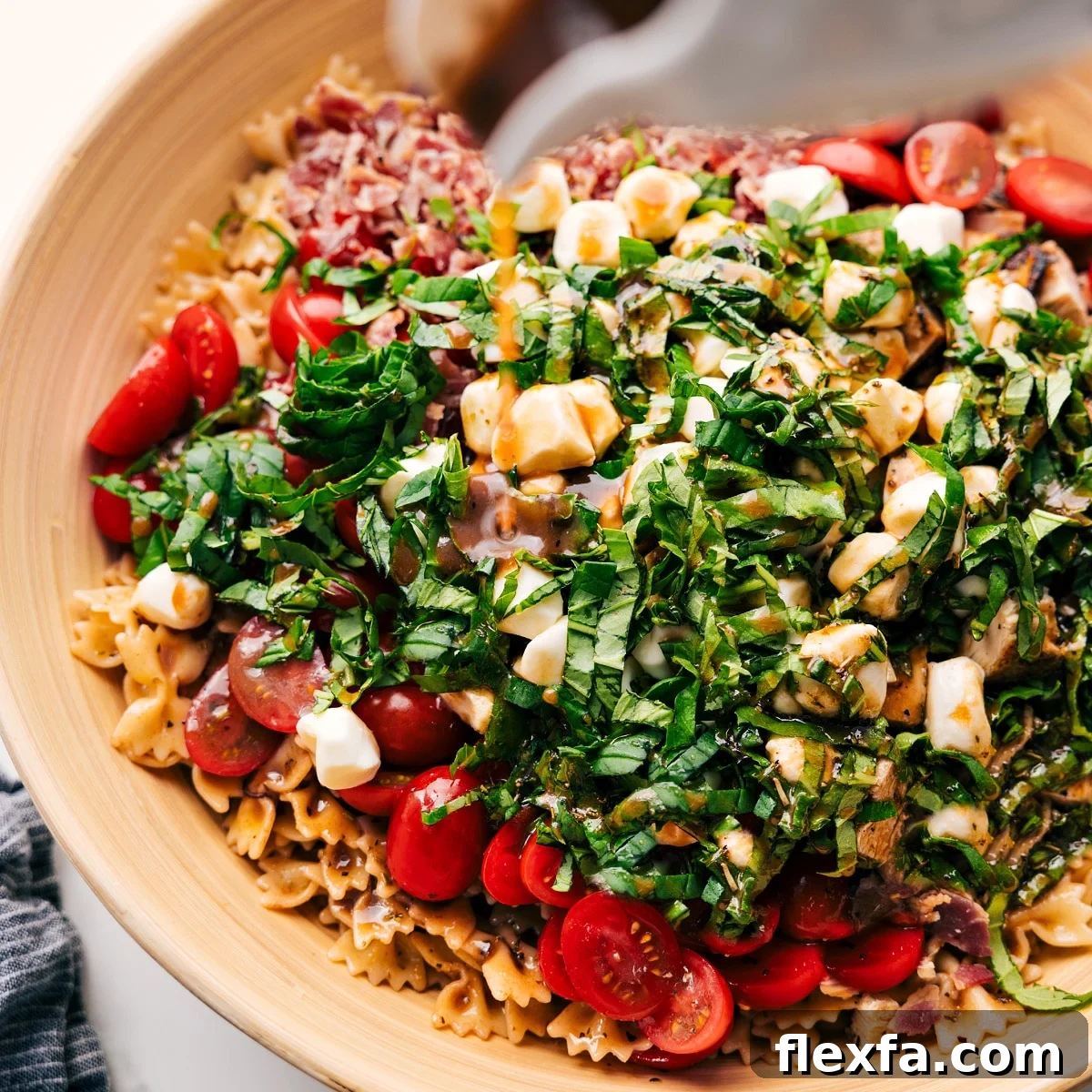 How To Make This Caprese Pasta Salad Dressing being poured over Caprese Pasta Salad in a large bowl before being tossed together.