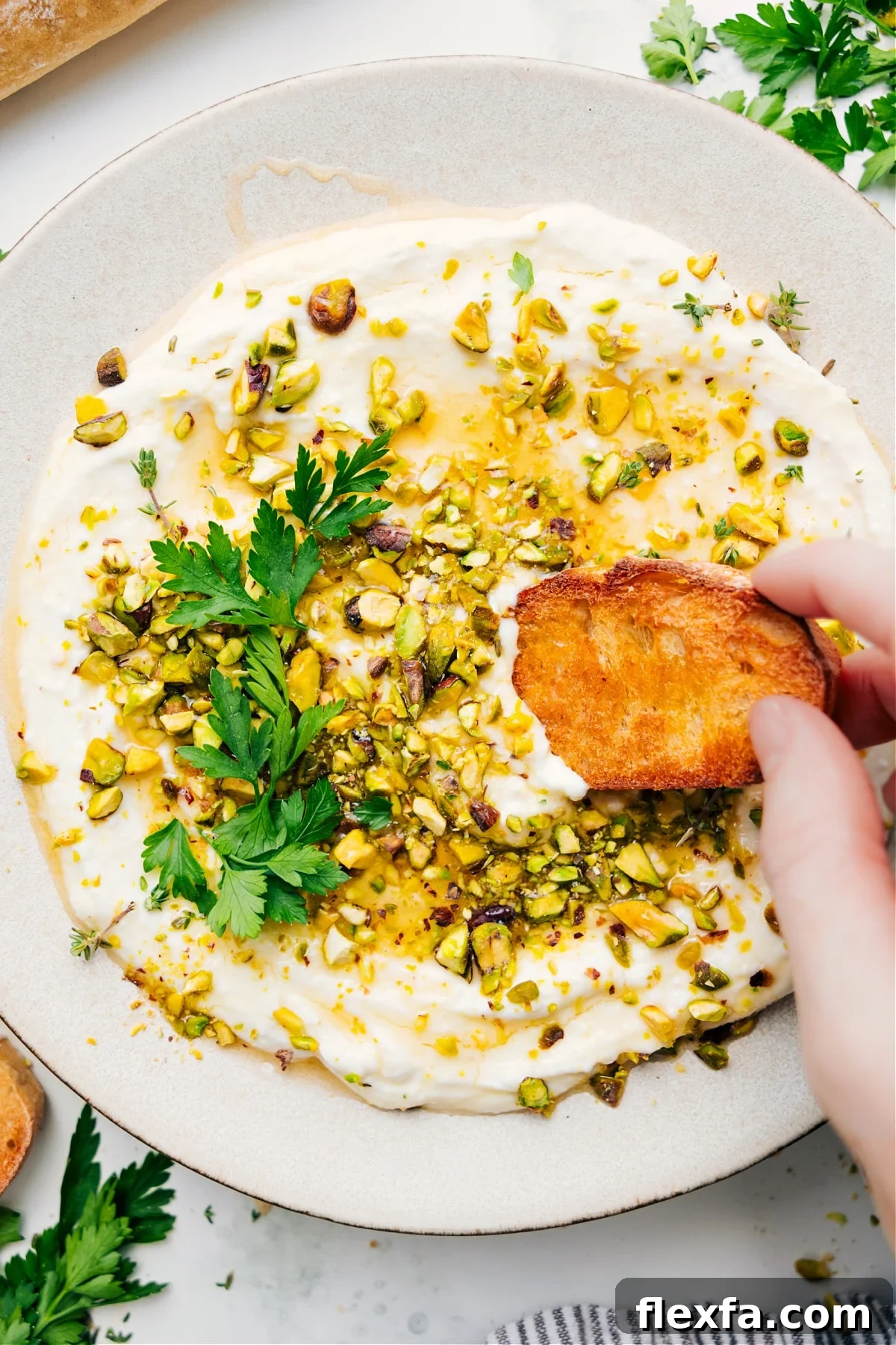 Whipped feta recipe with pistachios on top with a piece of bread dipping in.