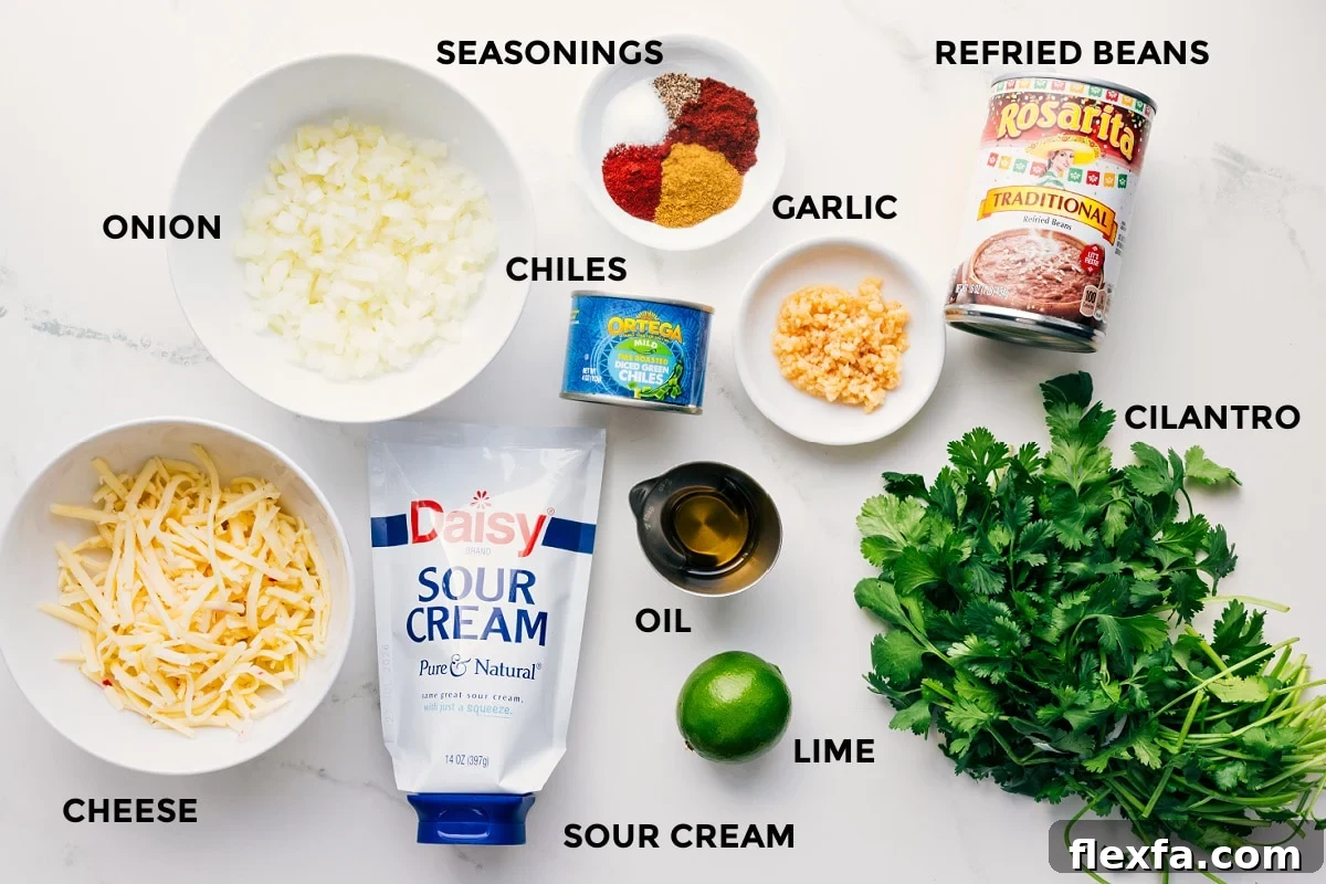 All the ingredients in this recipe prepped out for easy assembly including the cheese, onion, sour cream, lime, oil, chiles, seasoning, garlic, refried beans, and cilantro.