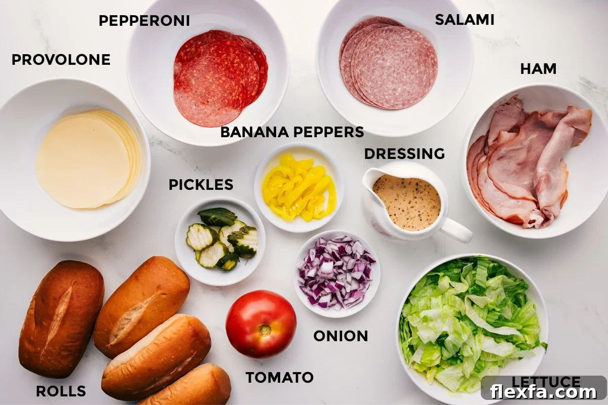 All the ingredients in this recipe prepped out for easy assembly including provolone, pepperoni, salami, ham, rolls, pickles, banana peppers, tomato, onion, dressing, and lettuce.