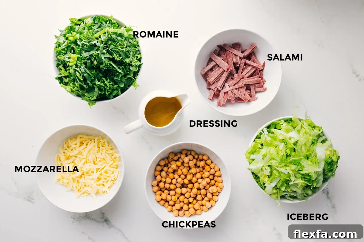 All the ingredients in this recipe prepped out for easy assembly including the romaine, mozzarella, salami, iceberg, chickpeas, and dressing.
