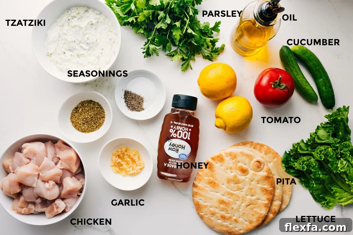 All the ingredients in this recipe prepped out for easy assembly including the tzatziki, seasonings, chicken, garlic, honey, pita, lettuce, tomato, cucumber, lemon, oil, parsley.
