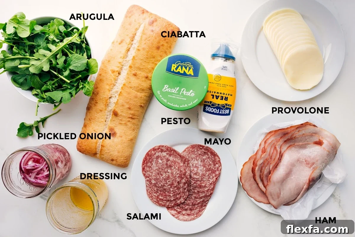All the ingredients in this recipe prepped out for easy assembly including the arugula, pickled onions, dressing, ciabatta, pesto, mayo, salami, ham, and provolone.