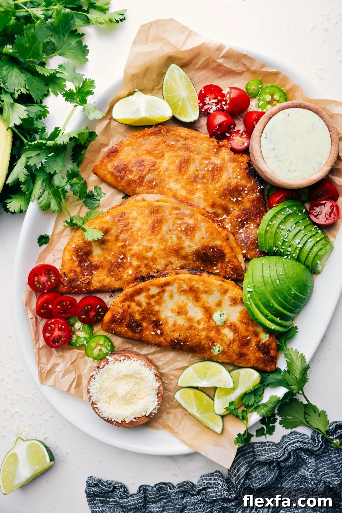 Crispy Beef Tacos on a tray with cilantro-lime sauce on the side, plus diced tomatoes, sliced avocado, lime wedges, and jalapeño slices for topping.