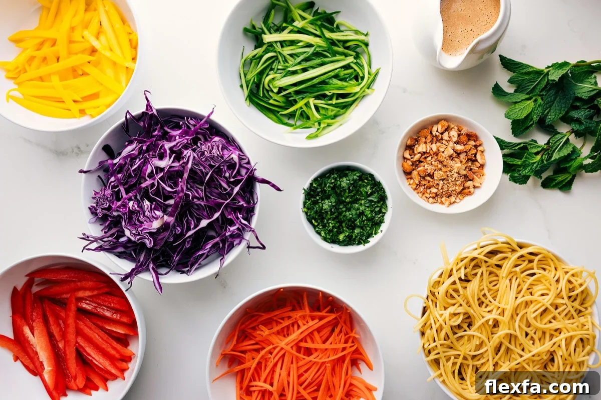 All the ingredients in this recipe prepped out for easy assembly including the peppers, cabbage, carrots, pasta, peanuts, dressing, herbs, and cucumbers.