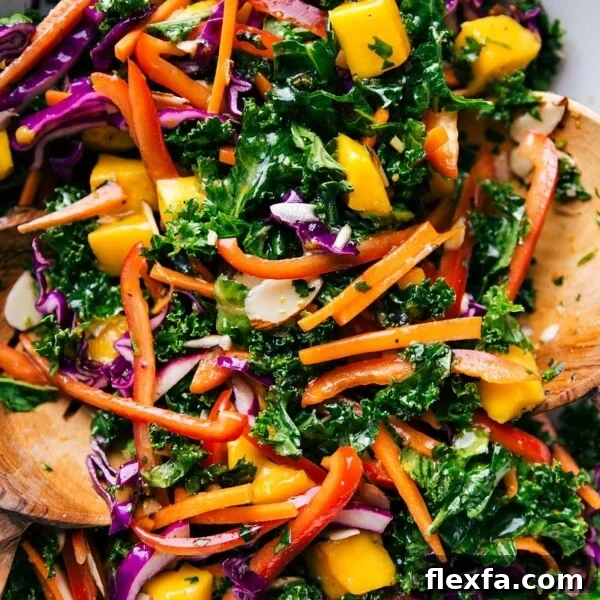 Colorful bowl of the completed kale salad recipe, complete with wooden serving spoons.