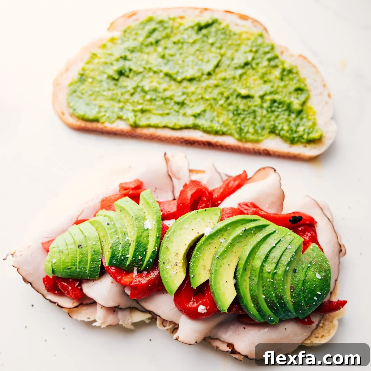 Preparing Panini Sandwich Recipes by layering turkey, cheese, avocado, roasted peppers, arugula, and pesto onto sliced bread.