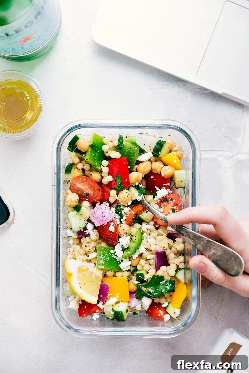 Greek couscous salad in a meal prep container with fresh vegetables.