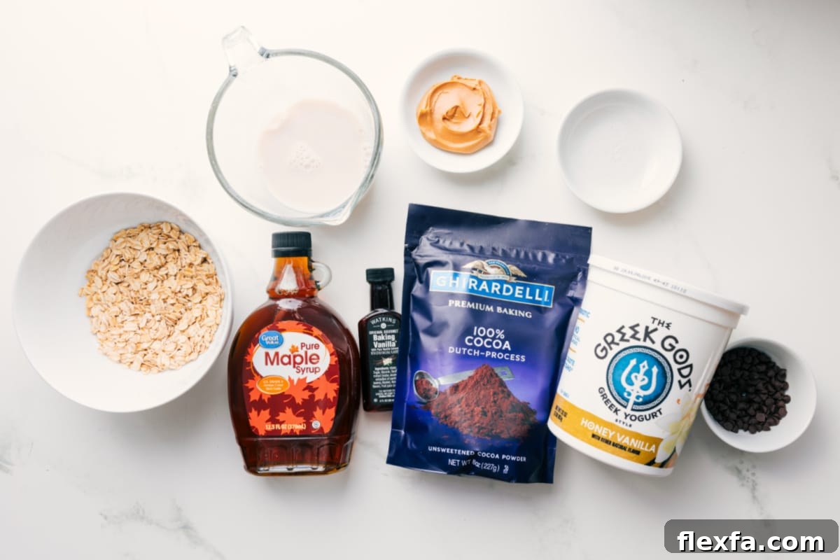 All the ingredients in this recipe prepped out for easy assembly including the oats, milk, maple syrup, cocoa powder, vanilla, yogurt, chocolate chips, peanut butter, and salt.