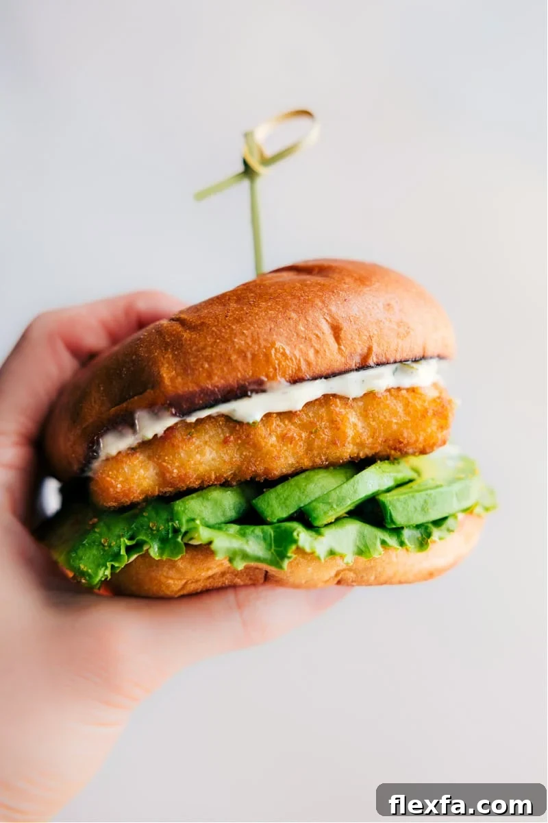 Fish sandwich with flaky fish, avocado, and lemon sauce on a toasted brioche bun.