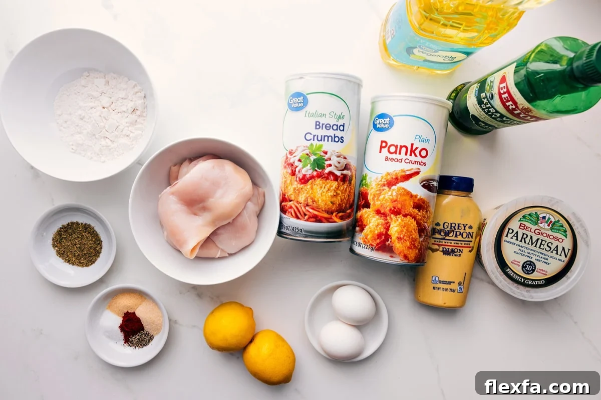 All the ingredients in this recipe prepped out for easy assembly including the flour, seasonings, chicken, lemon, egg, bread crumbs, dijon, parmesan, and oil.