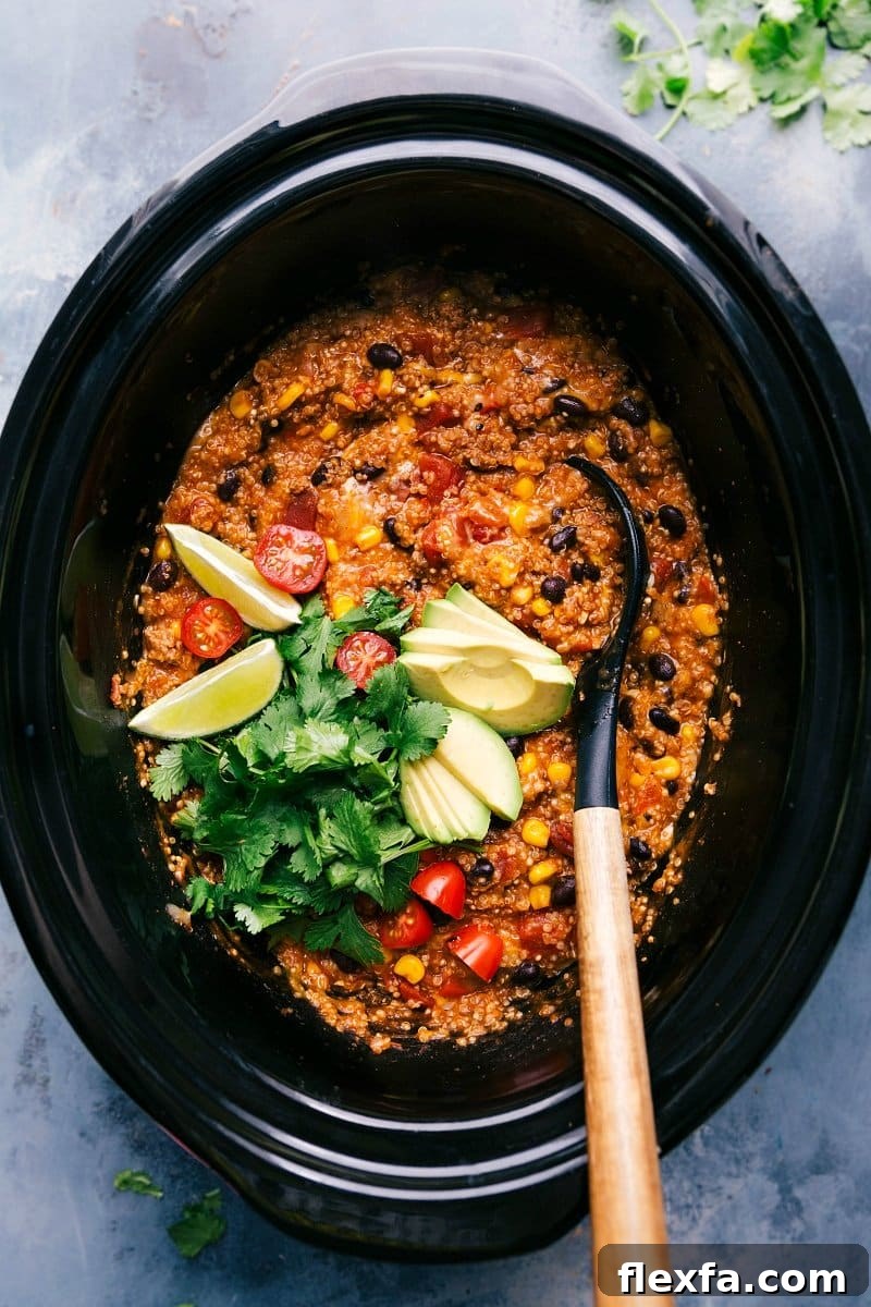 Easy crockpot meals featuring crockpot quinoa enchilada freshly made, served with a spoon and garnished with cilantro, tomatoes, avocado slices, and lime wedges.